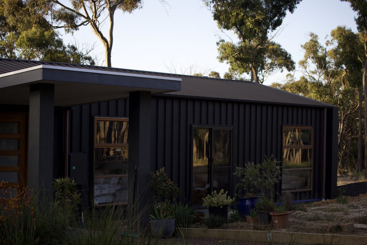 Home clad in dark vertical metal cladding with timber windows