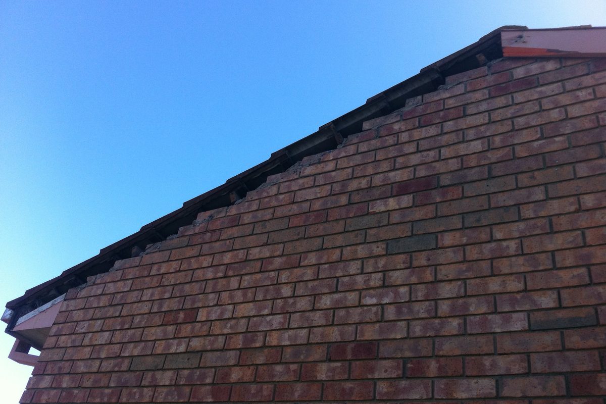 Weathered gable fascia on a brick home before JFM replaced it
