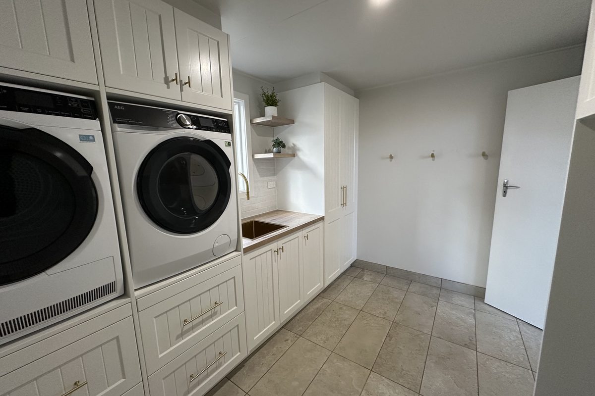 Renovated laundry with stacked machines, shaker cabinets and a timber bench