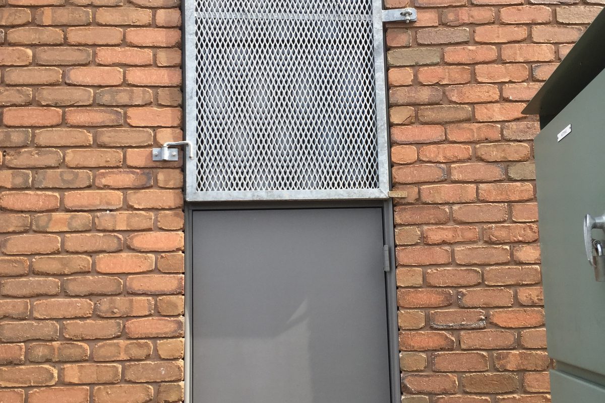 Steel door with a mesh vent set into a brick wall