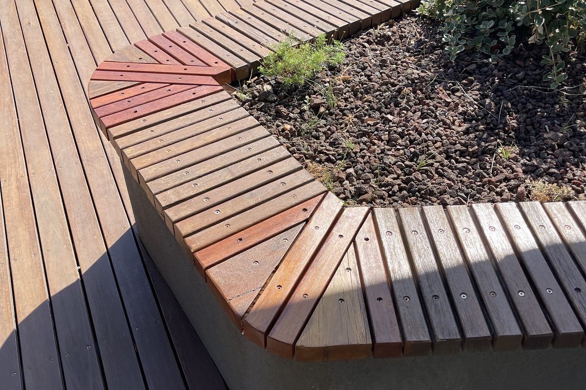 Curved timber seating around a garden bed rebuilt by JFM