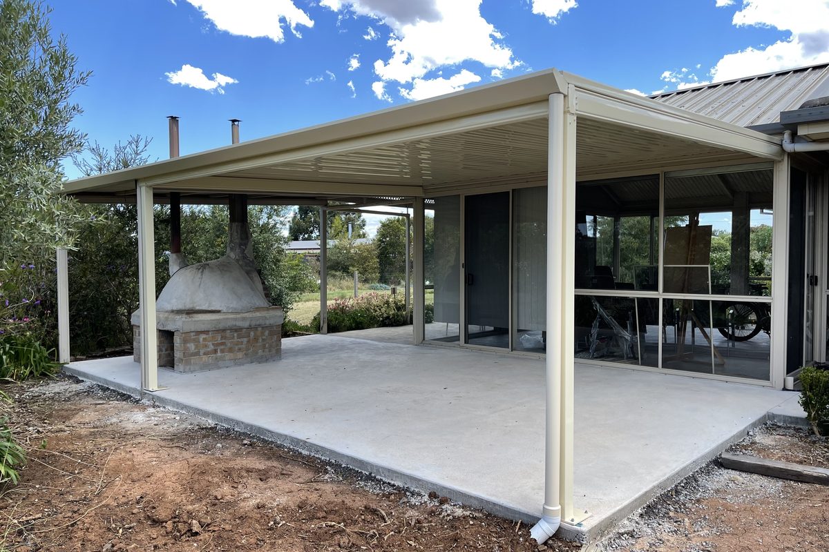 Steel-roofed verandah over a new concrete patio with an outdoor fireplace, built by JFM