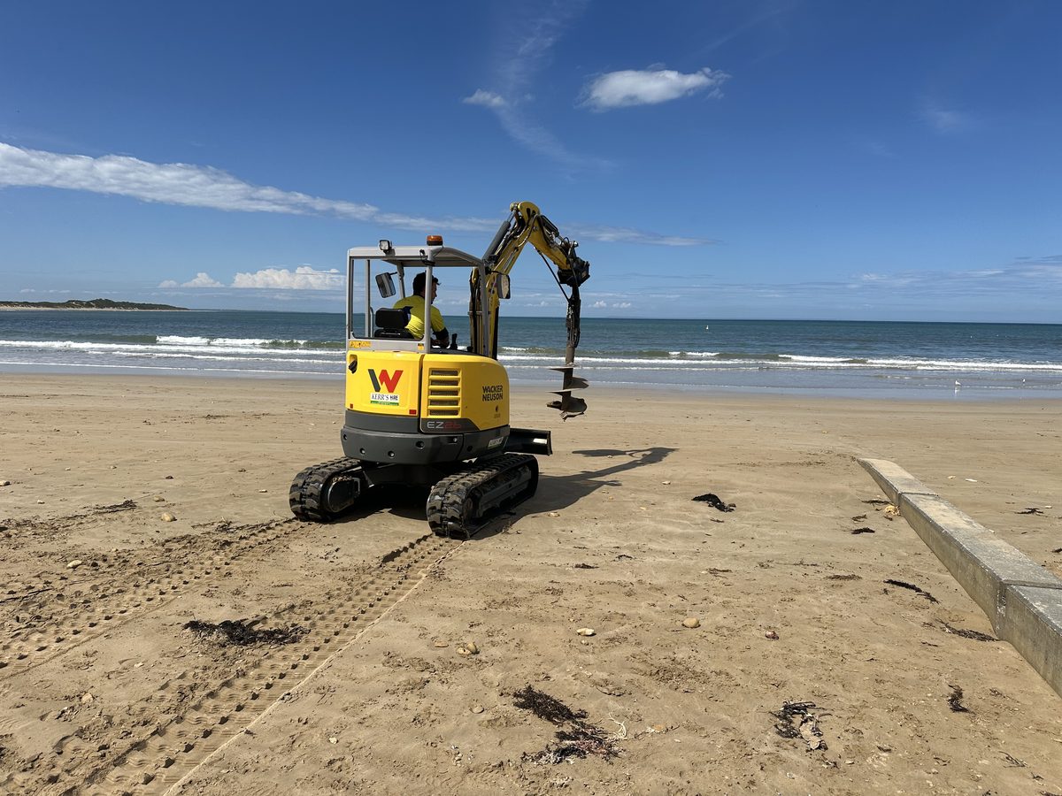 An excavator augering post holes into the beach sand for the ramp pylons
