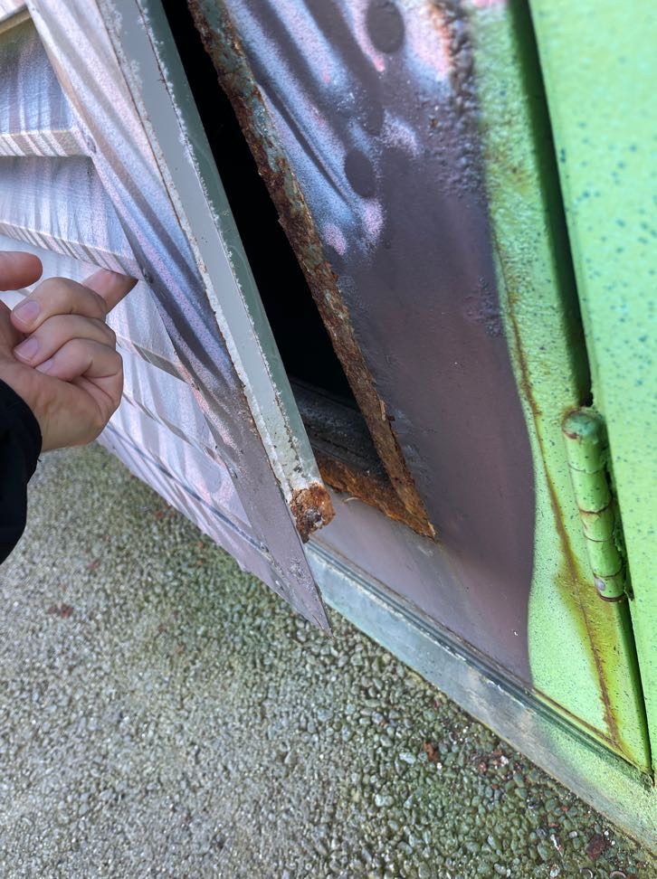 Rusted, corroded steel door skin lifting away from the frame